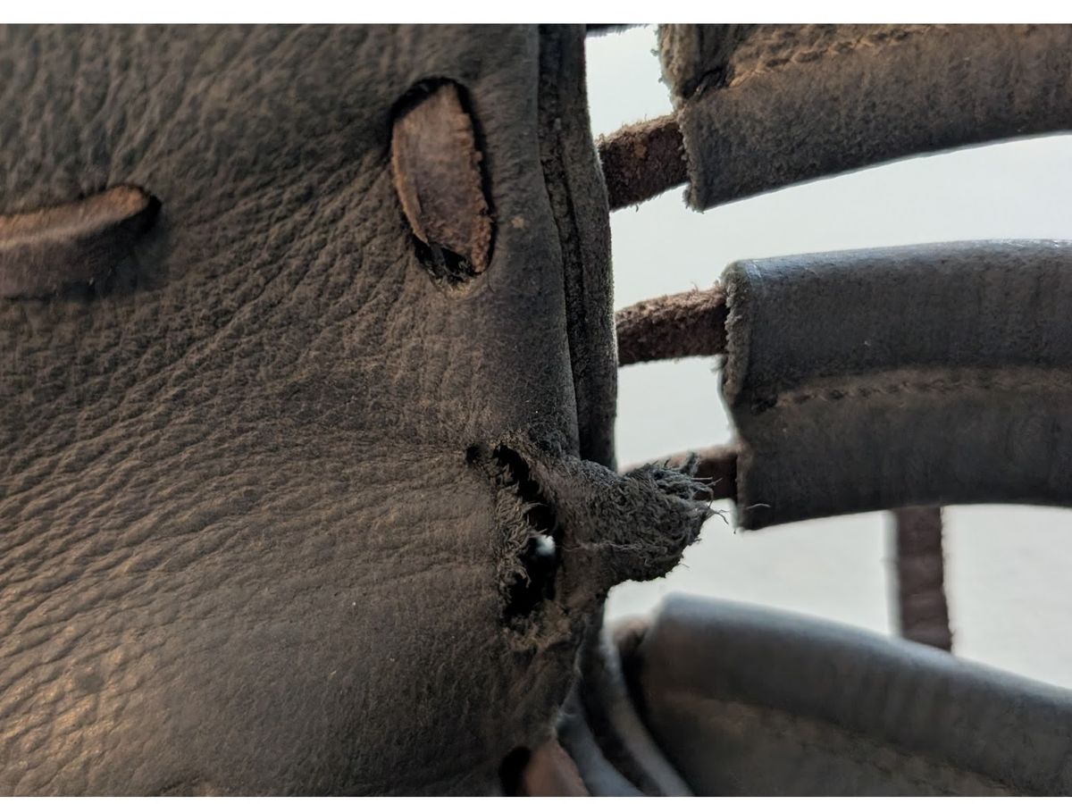 Torn lace hole in a black Rawlings first base mitt before repair